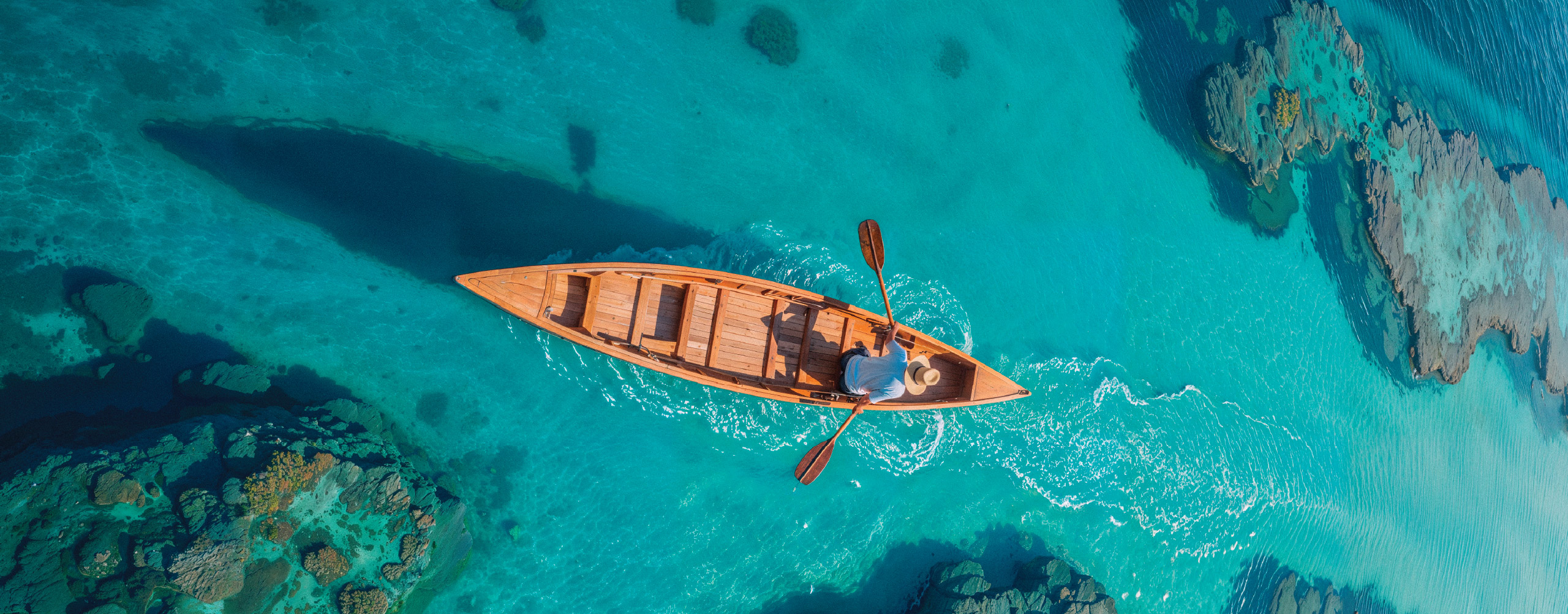 Aerial view of a wooden boat floating on crystal-clear turquoise waters during a Zanzibar beach holiday.