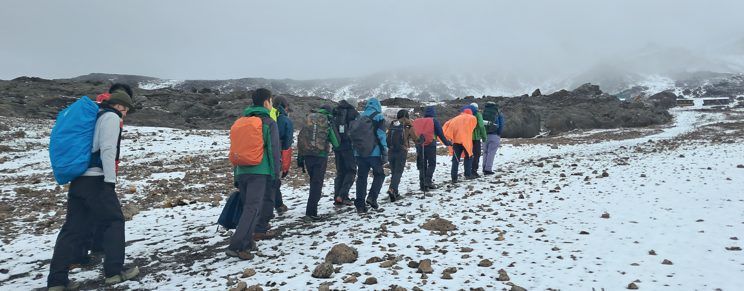 Group of hikers trekking through snowy mountain terrain under cloudy skies