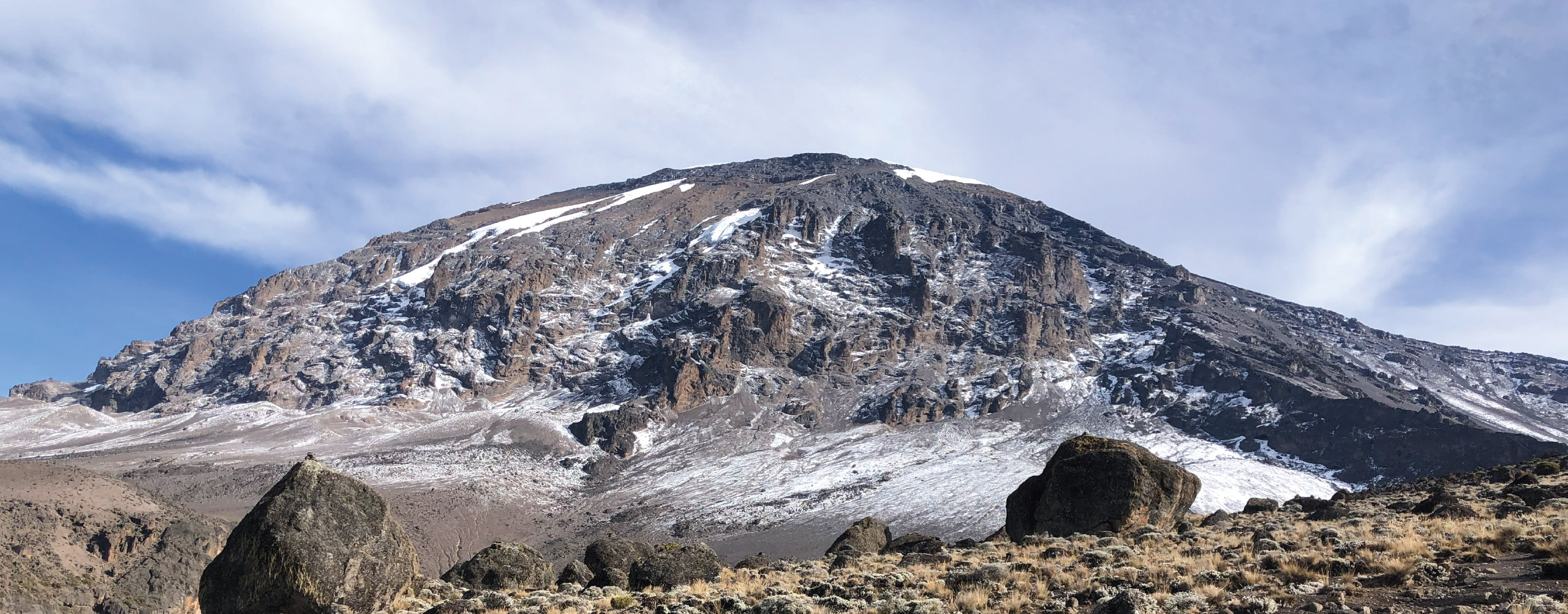 Snow-dusted mountain peak with rocky slopes under a partly cloudy sky