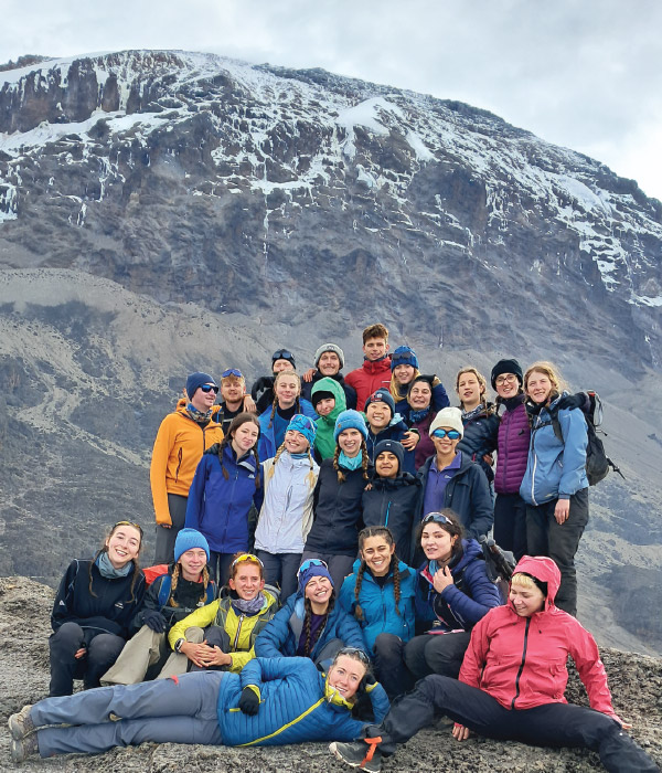 Group of climbers celebrating together on Mount Kilimanjaro with snow‑covered slopes in the background