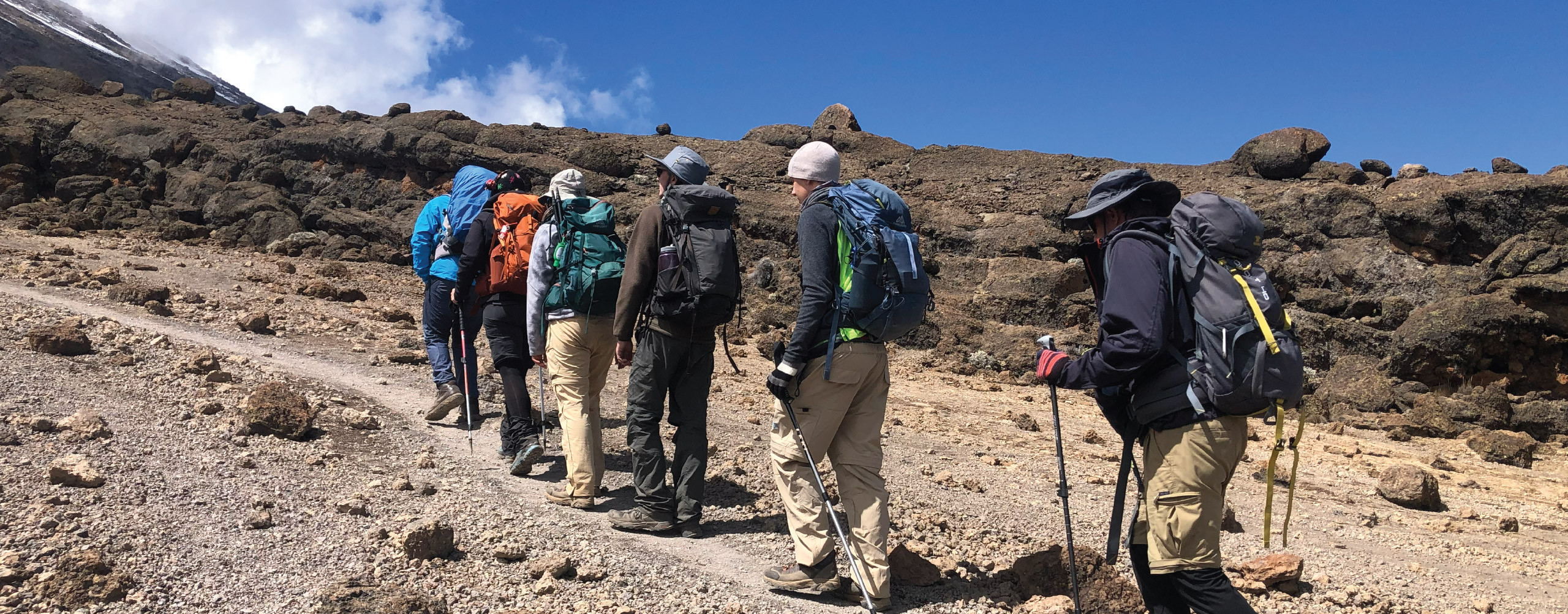 Group of hikers trekking a rocky mountain trail under a clear blue sky